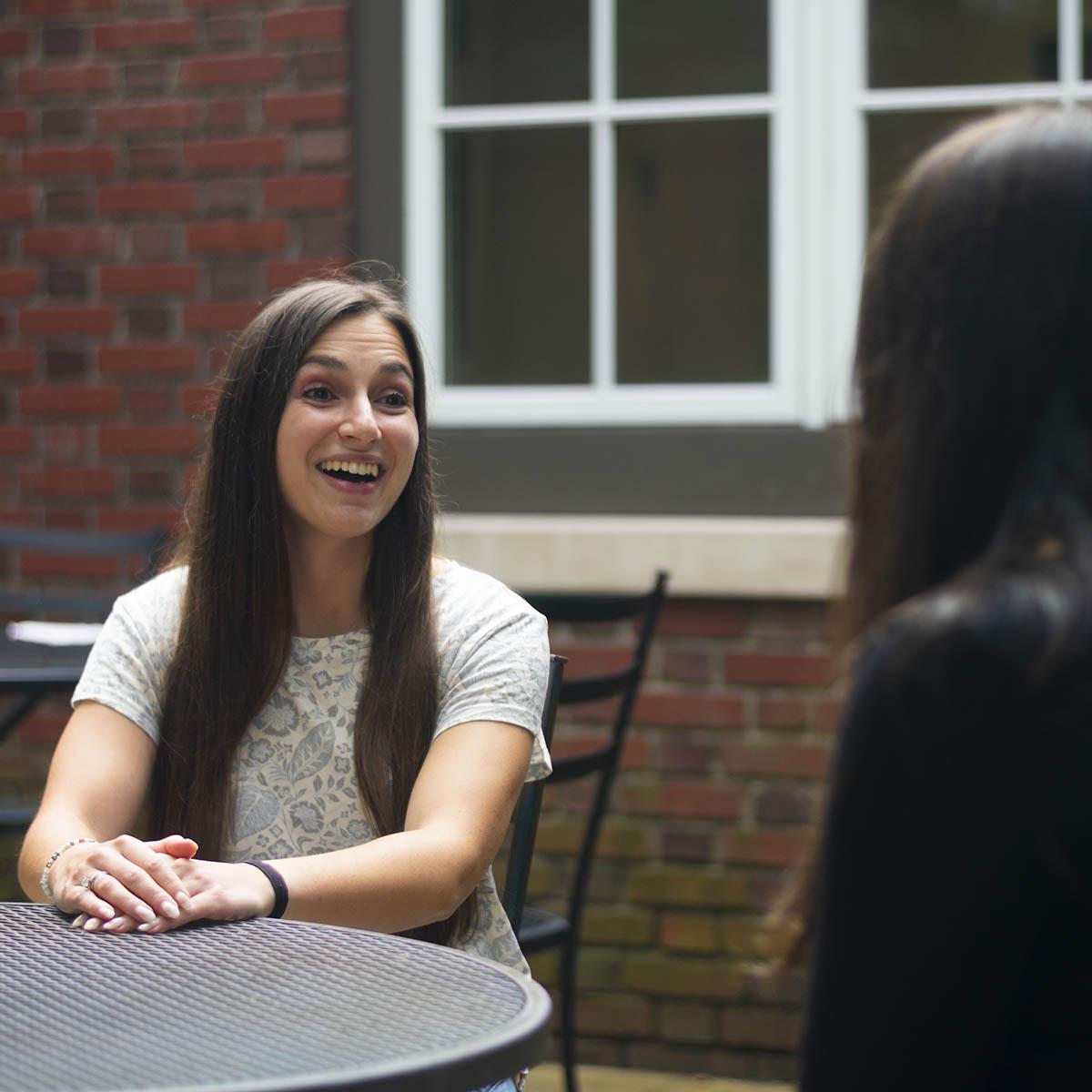 Photo of a success coach smiling and speaking with a student at an outdoor table